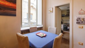 A dining area with a table set for four, a window with a view of a building, and a kitchen visible through an open door.