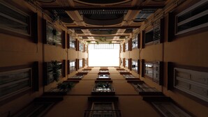 A corridor with multiple windows and plants, leading to a bright central area.