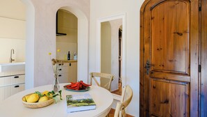 Uma sala de jantar com uma mesa redonda, cadeiras, uma tigela de frutas e um livro.