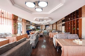 A spacious hotel lobby with seating areas, a kitchen in the background, and a wooden wall with plants. - Pangye Hotel (Dayao)