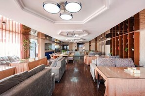 A spacious hotel lobby with seating areas, a kitchen in the background, and a wooden wall with plants. - Pangye Hotel (Dayao)