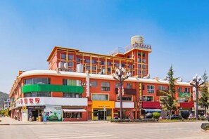A multi-story hotel with a curved facade, multiple ground-level shops, and a clear sky. - Pangye Hotel (Dayao)