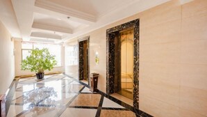 A hotel lobby with a polished marble floor, a potted plant, and a large mirror.