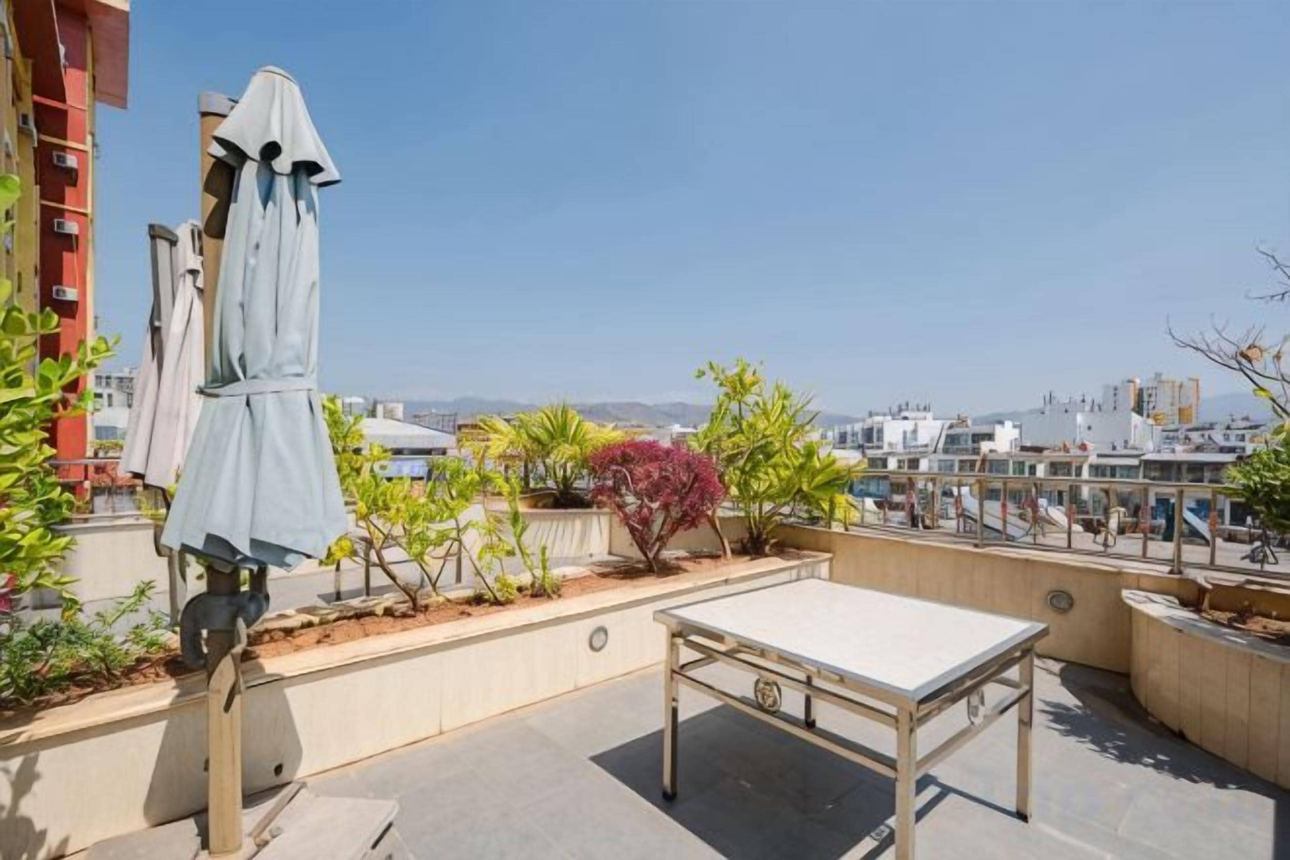 Terraza en la azotea con mesa y sillas, un rincón cubierto para sentarse y vistas de la ciudad.