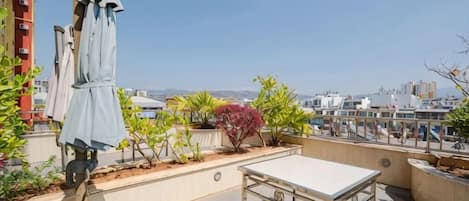 Une terrasse sur le toit avec une table et des chaises, un espace salon couvert et une vue sur le paysage urbain.