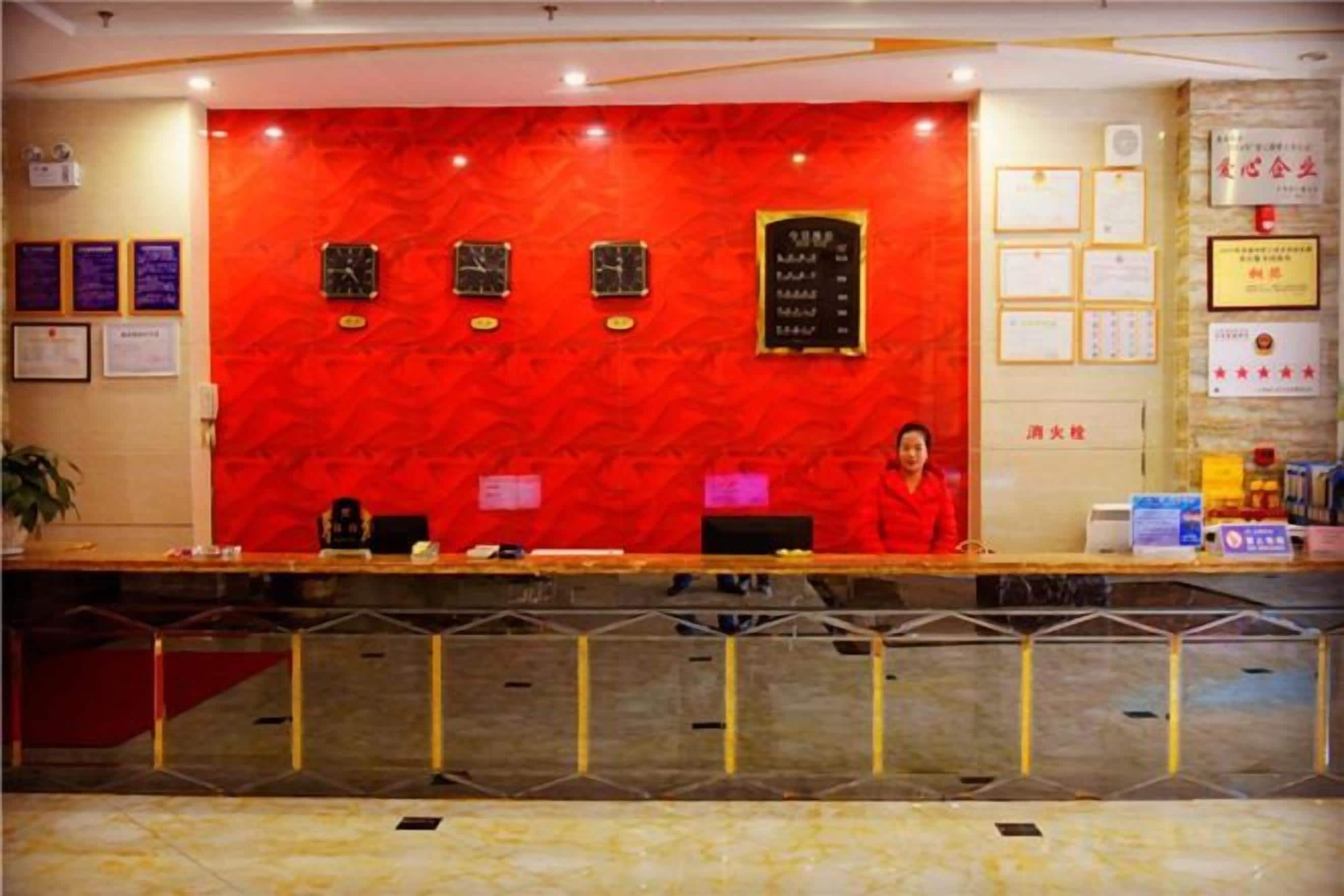 A reception desk with a red wall, framed certificates, and a woman standing behind it.
