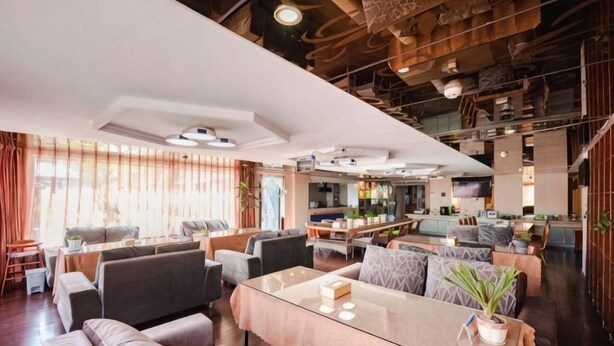 A modern hotel lobby with seating areas, a glass coffee table, and a kitchen in the background.