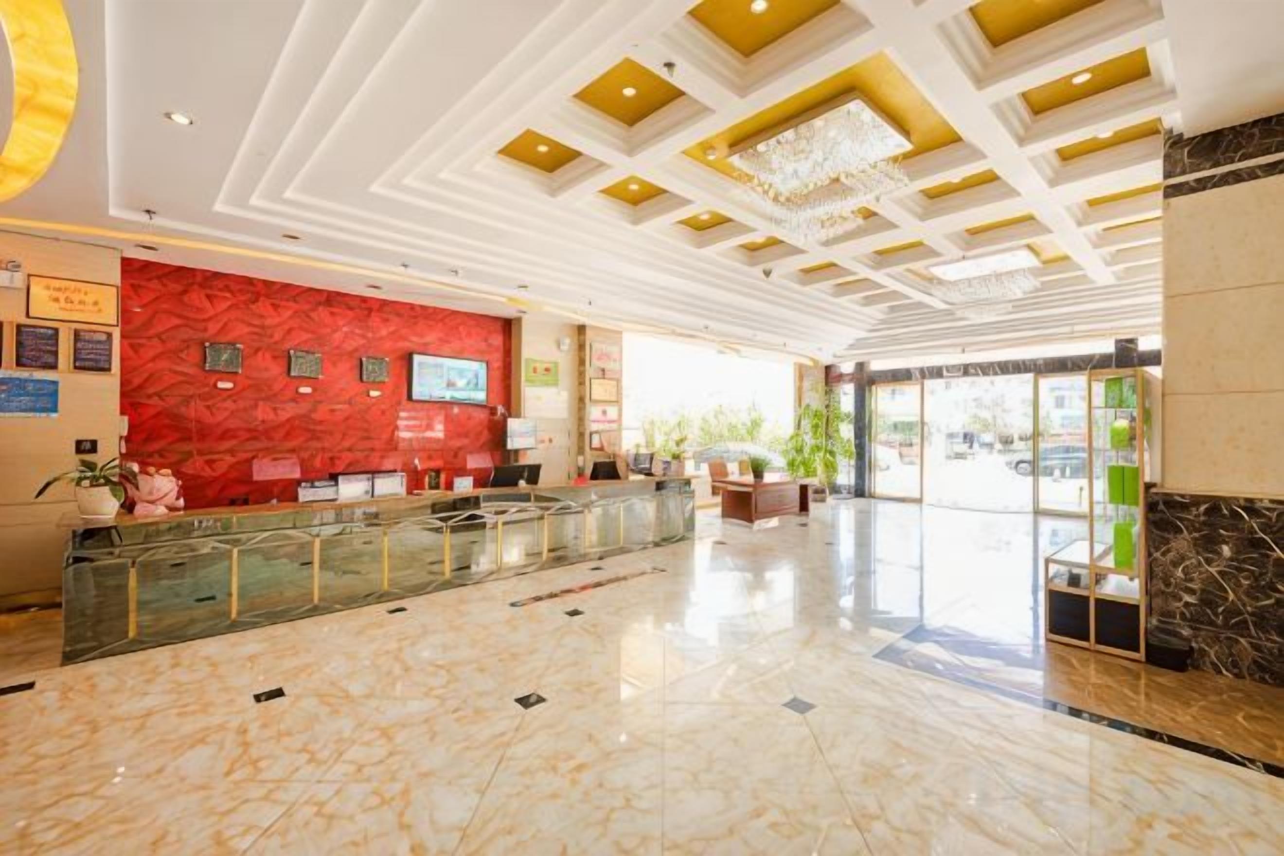 A hotel lobby with a reception desk, a chandelier, and a marble floor.