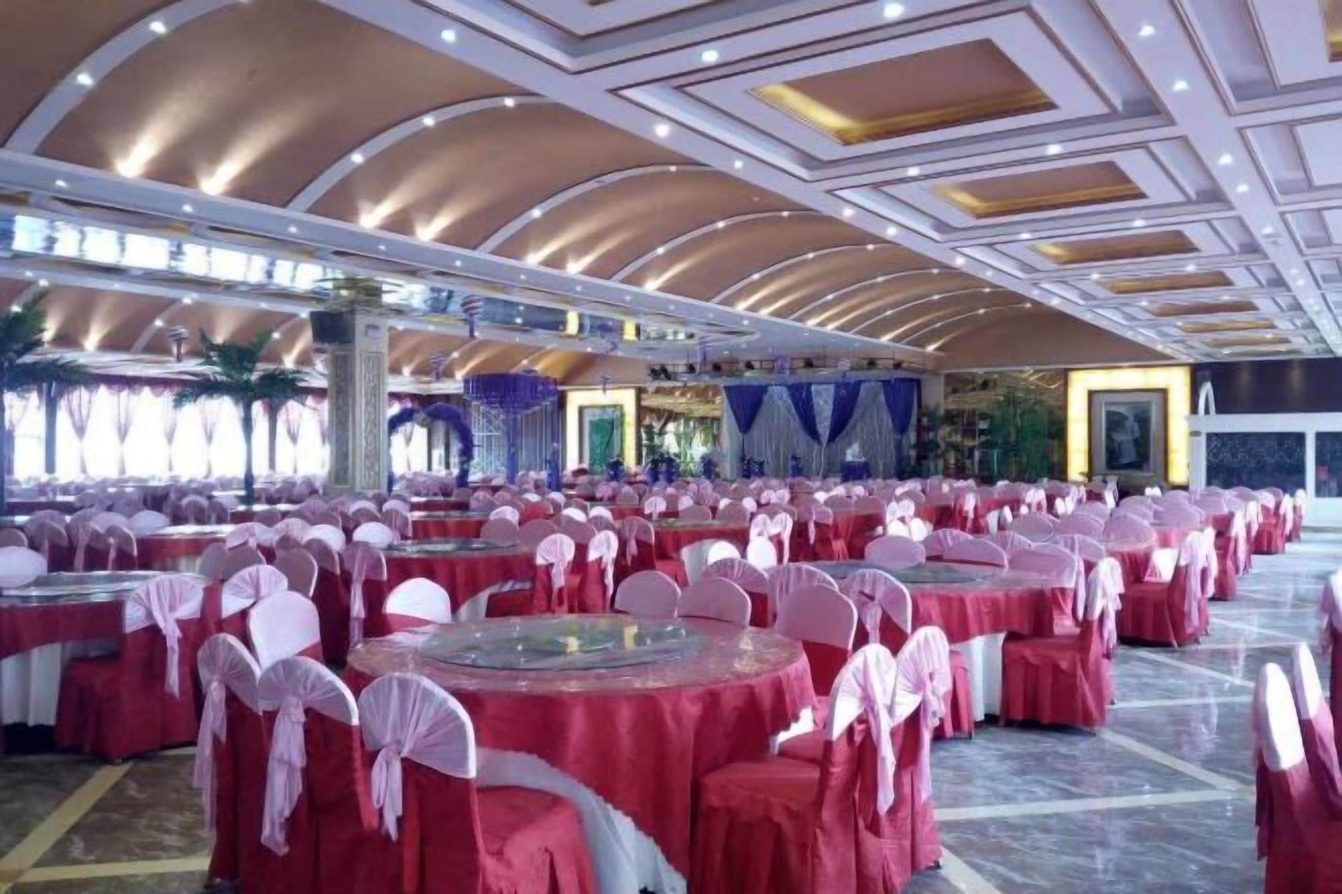 A banquet hall with round tables covered in red tablecloths and white chairs, arranged in rows.