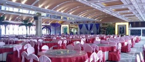 A banquet hall with round tables covered in red tablecloths and white chairs, arranged in rows.