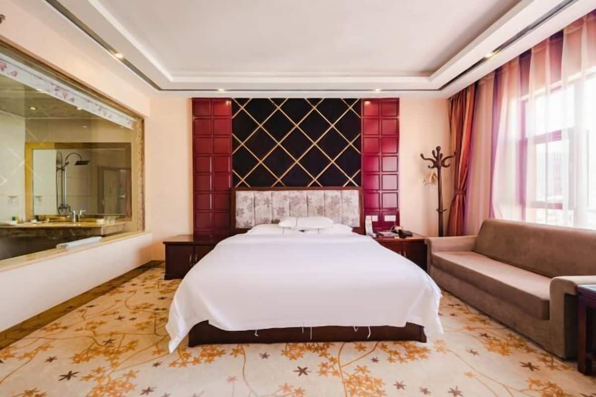 Ein Hotelzimmer mit einem großen Bett, einer Couch, einem Spiegel und einem Fenster mit Vorhängen.