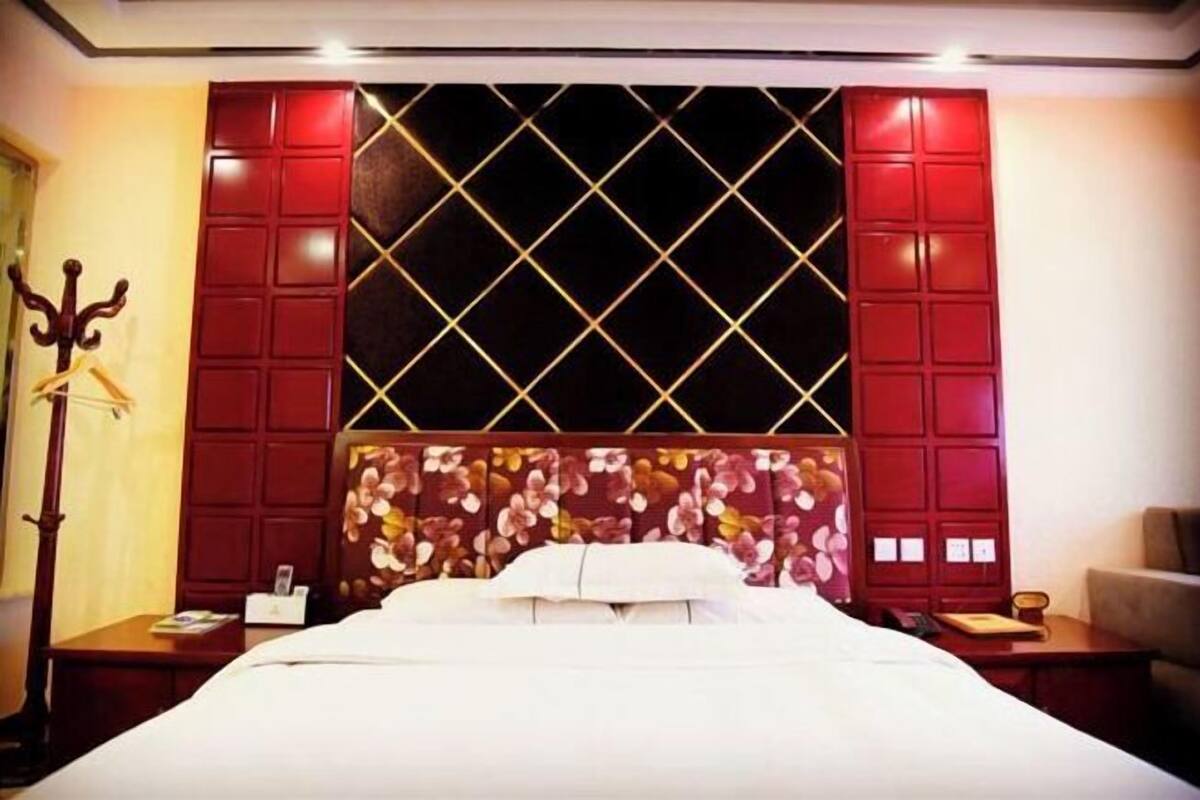 Ein Hotelzimmer mit einem großen Bett, einem Blumenmuster an der Kopfteil, einem dunklen Fenster und einer roten Akzentwand.