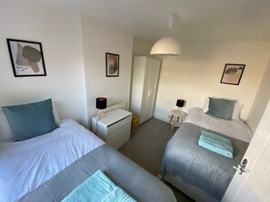 Een hotelkamer met twee eenpersoonsbedden, een nachtkastje met een lamp, een garderobe en een spiegel.