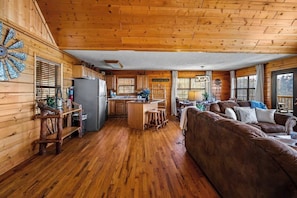 A wooden cabin interior with a kitchen, dining area, and a large brown sofa.
