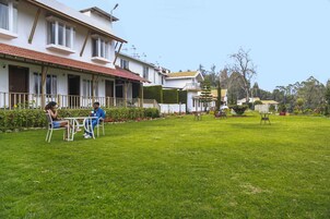 A courtyard with a white building, a grassy lawn, and a few outdoor tables and chairs.