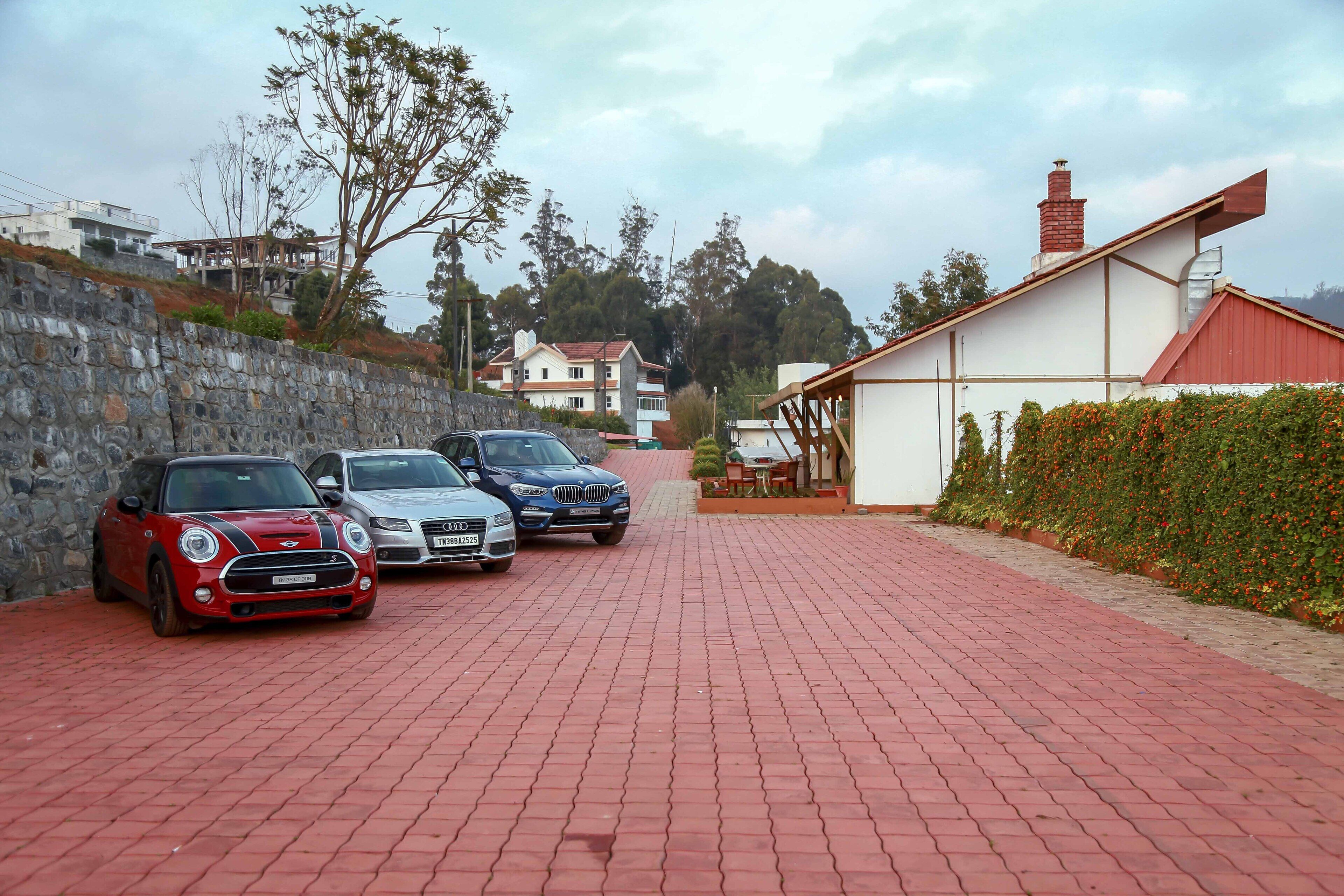 A paved driveway with parked cars, a stone wall, and a building with a red roof.