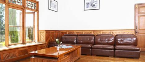 A living room with a wooden coffee table, leather sofa, and large windows.