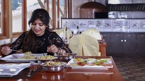 Un coin repas avec une table dressée pour deux personnes, où l’on peut admirer une variété de plats et, au fond, un four à pizza.