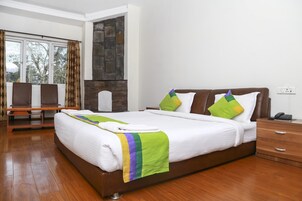 A modern hotel room with a large bed, wooden floor, a stone fireplace, and a seating area with chairs and a table.