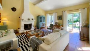 A living room with a sofa, coffee table, fireplace, and a view of the outdoors. - Villa for 10 • Pool • 5 Suites • Grimaud (Grimaud)