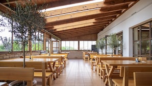 A spacious indoor dining area with wooden tables and benches, large windows, and potted plants. - Amenity Penzion Horní Věstonice (Horní Vestonice)