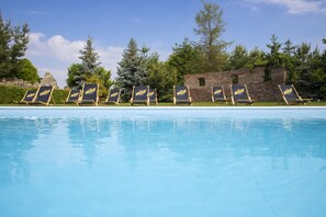 Piscina com espreguiçadeiras e um muro de tijolos ao fundo.