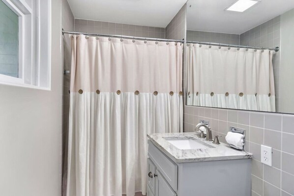 A bathroom with a shower curtain, a sink, and a mirror.