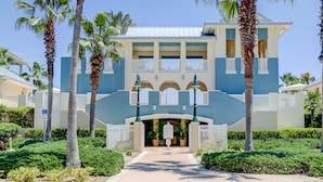 Een hotelgevel in het blauw, met witte balkons en palmbomen.