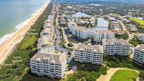 Luchtbeeld van een kustresort met accommodaties direct aan het strand, een jachthaven en omliggend groen.