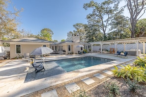 A backyard with a swimming pool, outdoor seating, and a covered patio area.