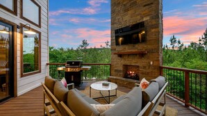 Eine überdachte Terrasse mit Gartenmöbeln, einem Kamin aus Stein und einem Grill.