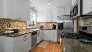 A modern kitchen with white cabinets, a stainless steel refrigerator, a microwave, and a gas stove.