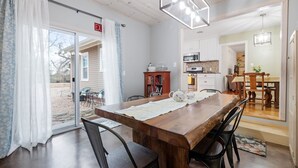 A dining area with a wooden table, black chairs, a chandelier, and a kitchen in the background.