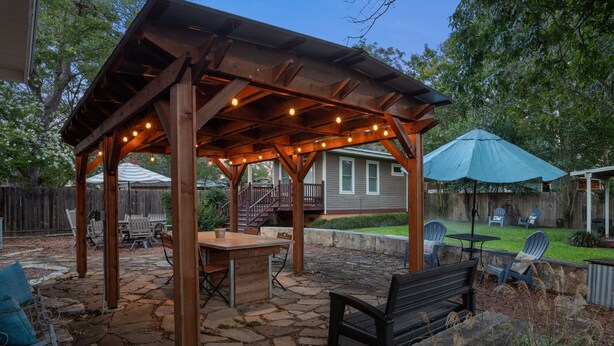 A covered outdoor patio with a stone floor, a wooden table, and chairs.