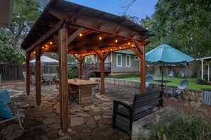 A covered outdoor patio with a stone floor, a wooden table, and chairs. - Lovebirds Getaway 3 Bedroom Home by RedAwning (Fredericksburg)