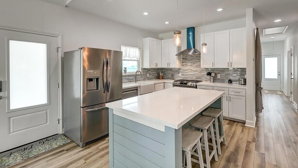 A modern kitchen with a stainless steel refrigerator, a central island with bar stools, a gas stove, and white cabinetry.