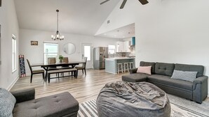 A spacious living area with a gray sofa, ottoman, and a dining table with chairs. A ceiling fan and chandelier are visible.