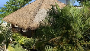 A thatched-roof structure surrounded by lush tropical vegetation. - Family Comfort In Jamaica - Enjoy 7 Miles Of White Sand Beach! Villa by RedAwning (Negril)