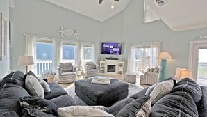 A spacious living room with a large gray sectional sofa, a ceiling fan, and a flat-screen TV mounted on the wall.