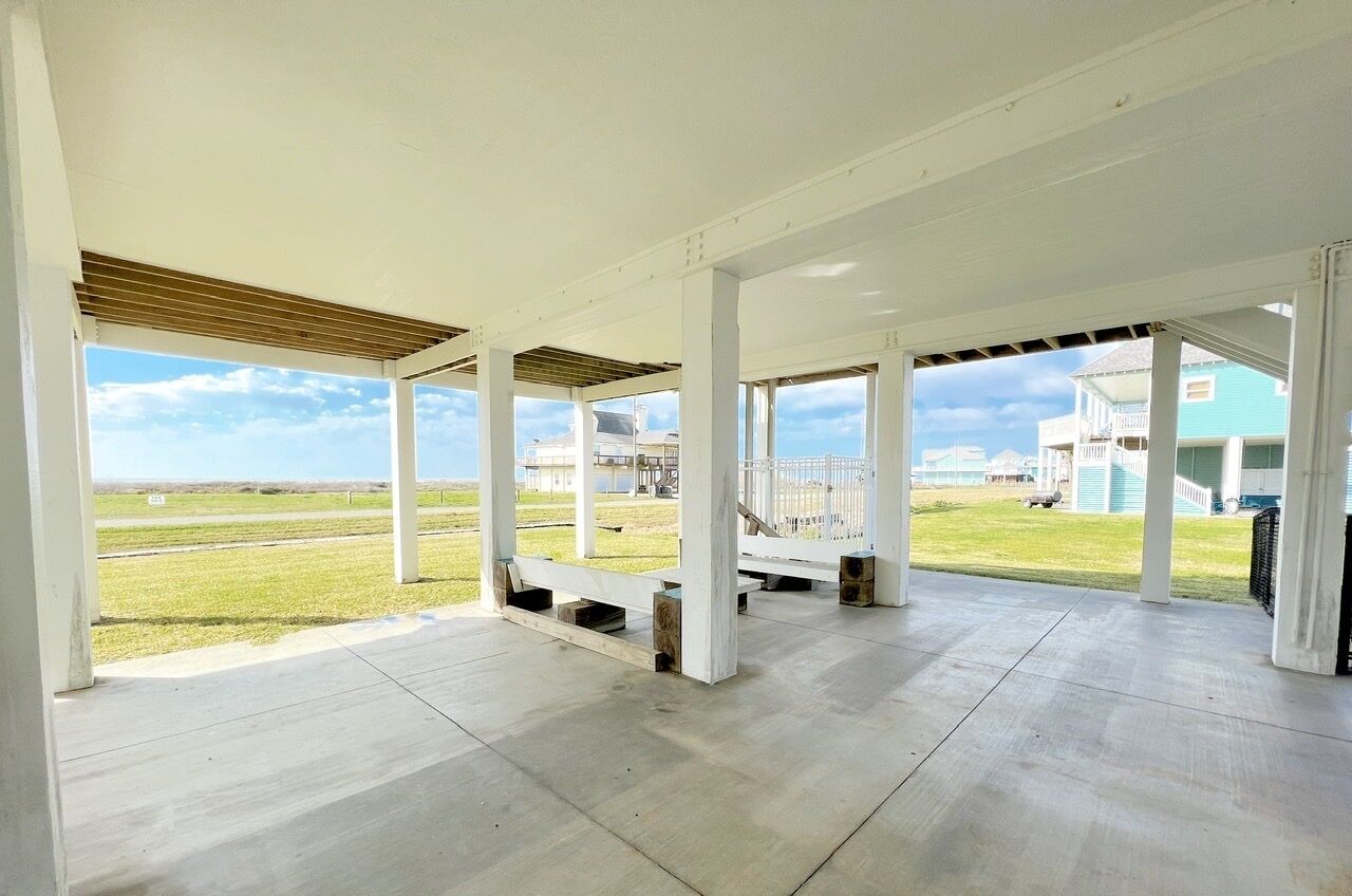 An open, covered outdoor area with a view of a grassy field and buildings in the background.