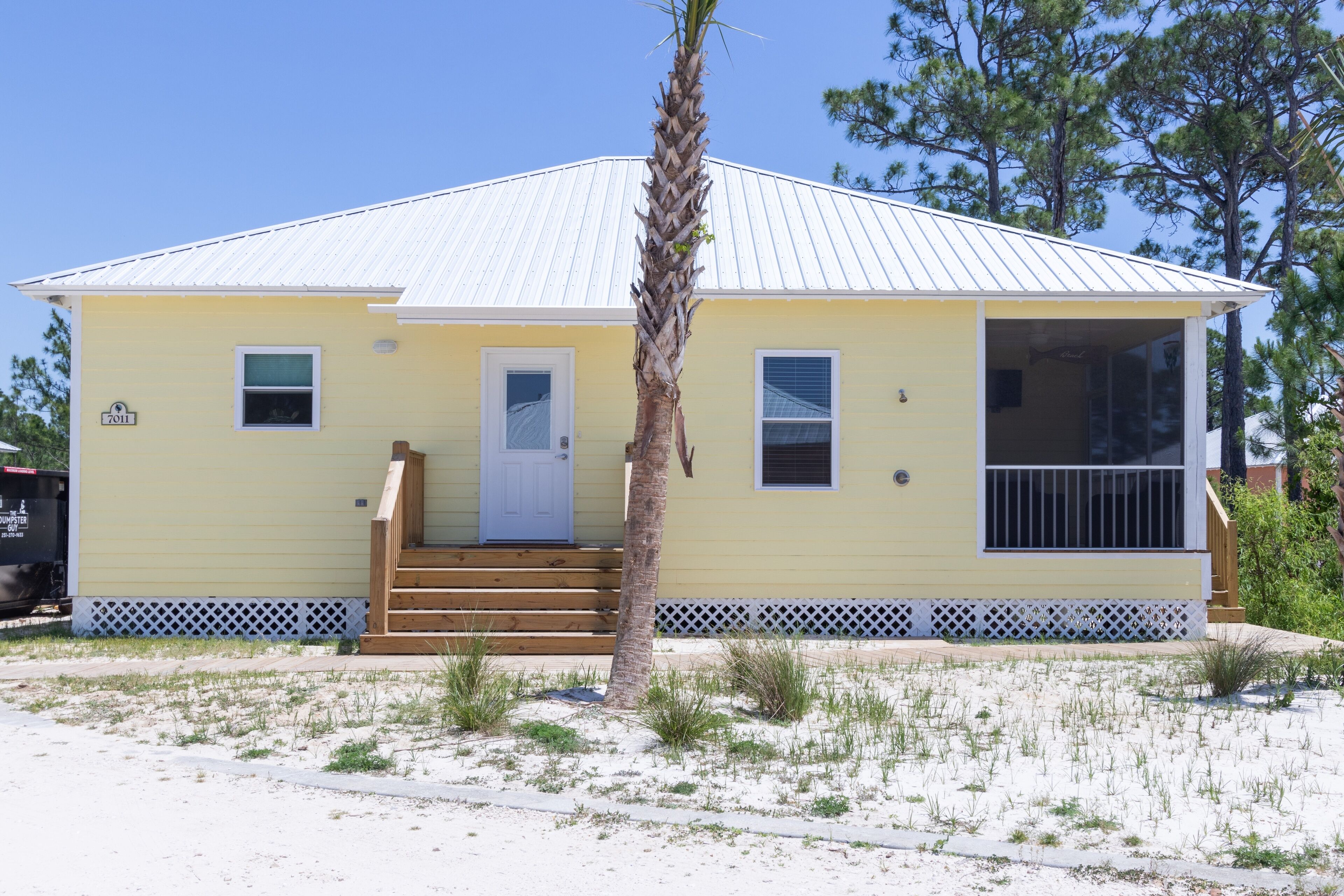 A yellow house with a white door, a small porch, and a palm tree in front.