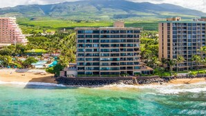 A beachfront hotel with multiple floors, a pool, and a view of the ocean and mountains.