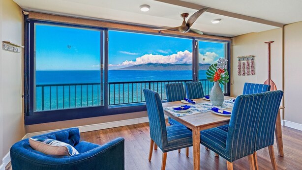 A dining area with a view of the ocean, a ceiling fan, and a table set for four.