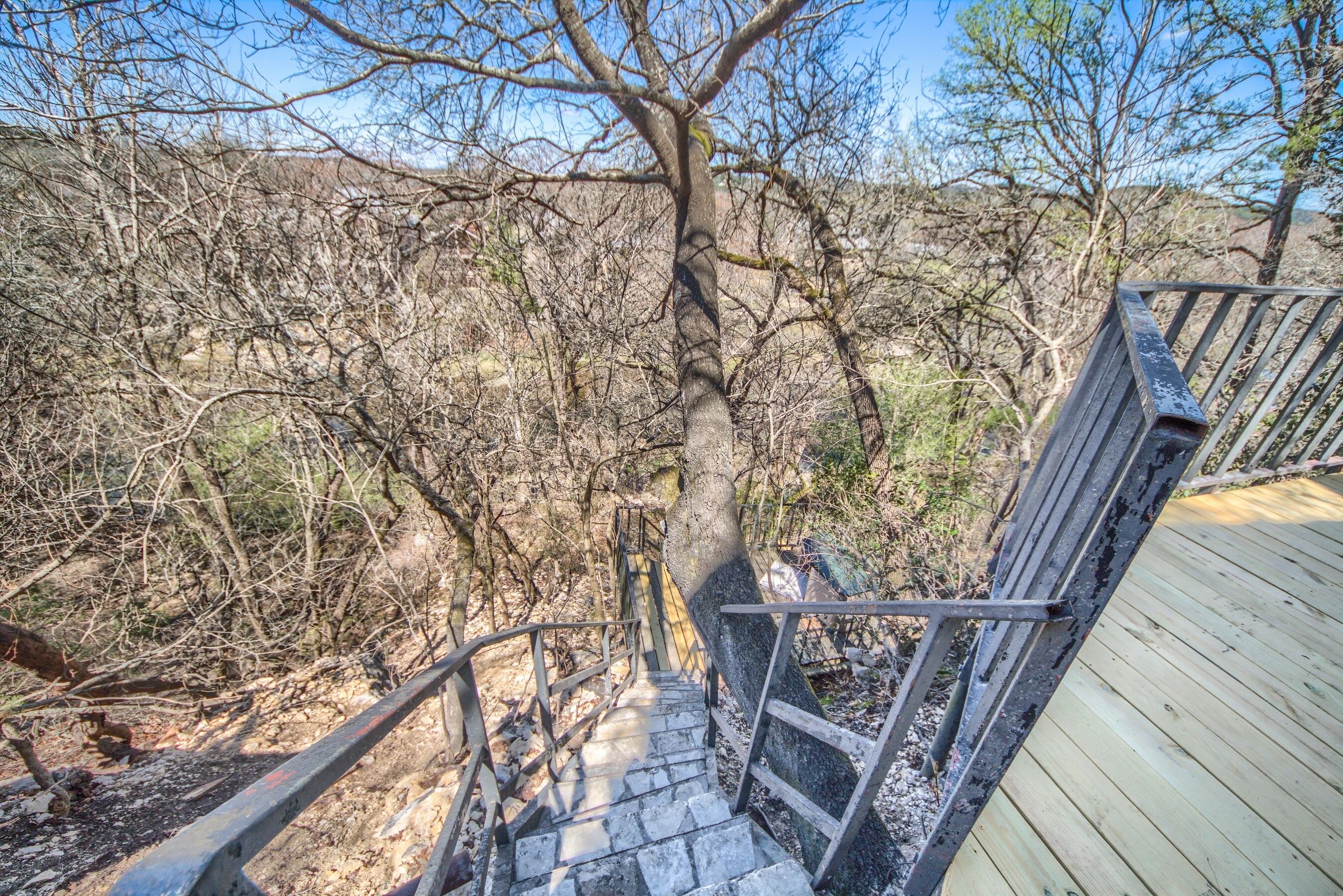 A wooden staircase leading up to a platform with a metal railing, surrounded by dry, leafless trees and a clear sky.