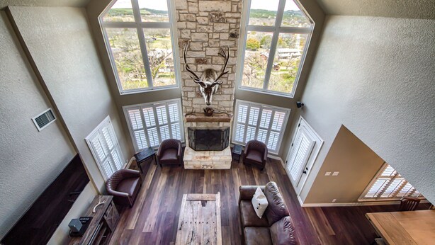 A spacious loft with a stone fireplace, large windows, and a high ceiling.