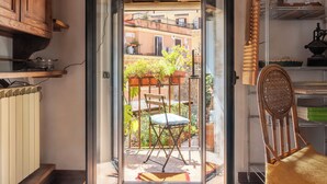 Una cocina con alacenas de madera, un radiador y vistas a un balcón con una silla y plantas en macetas.