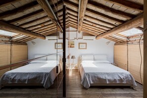 Une chambre avec deux lits, des poutres en bois au plafond et une fenêtre avec des stores.