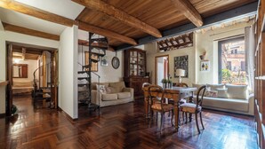 Amplia sala de estar con piso de madera y vigas a la vista, una mesa de comedor con sillas, un sofá y una escalera que conduce a otra habitación.