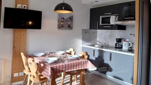 Una cucina compatta con elettrodomestici moderni, un'area pranzo con tovaglia a quadretti e un televisore a schermo piatto montato a parete.