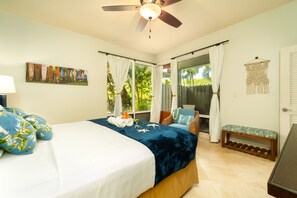 A bedroom with a bed, a ceiling fan, a window with curtains, a bench, and a wall-mounted macrame piece.